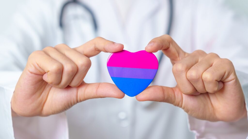 A doctor holding a heart with the bisexual flag 