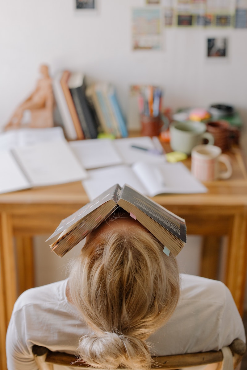 Person in front of a desk with a book on her face