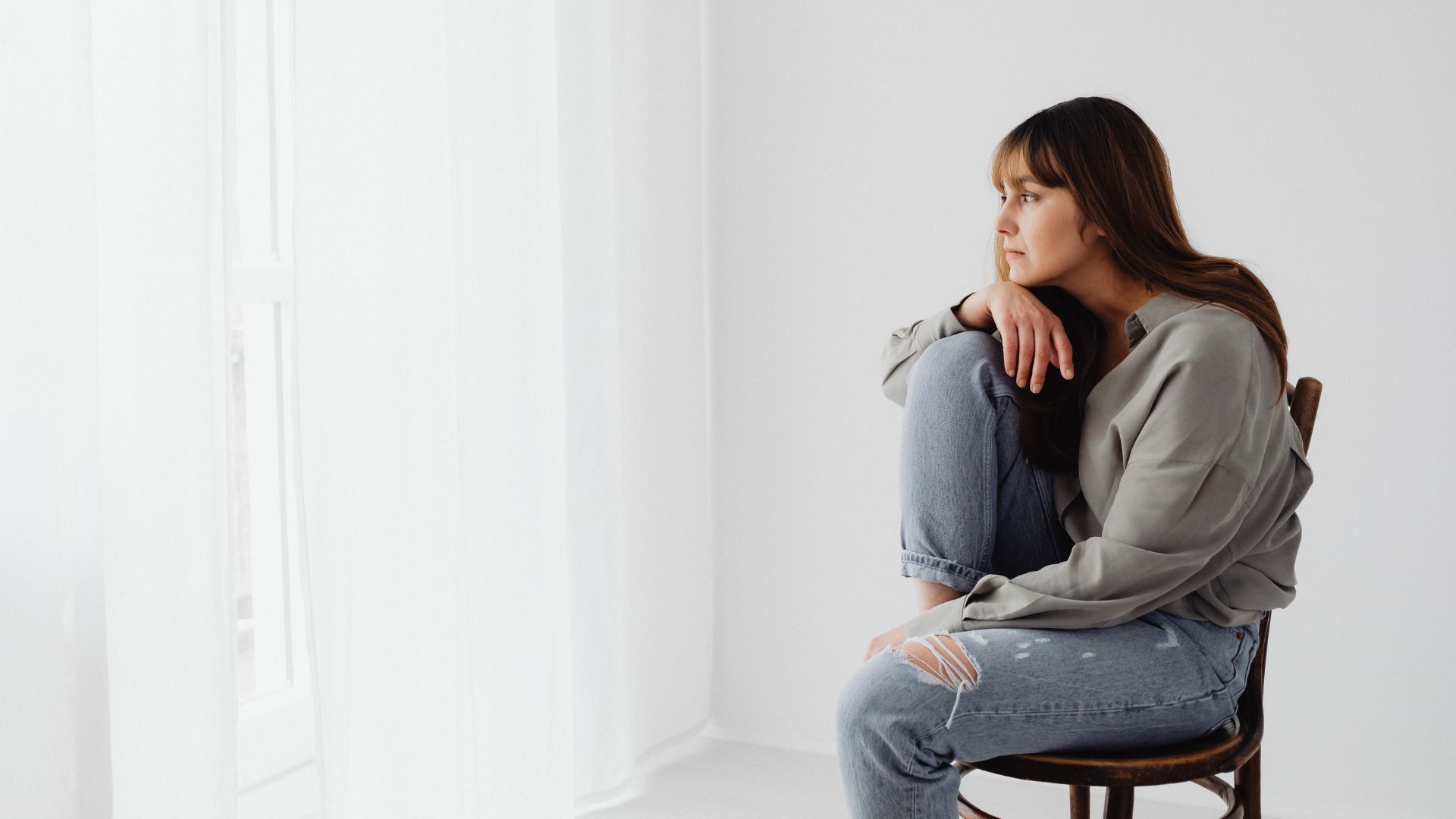 A Woman in Gray Long Sleeves Sitting on Chair Looking Pensive