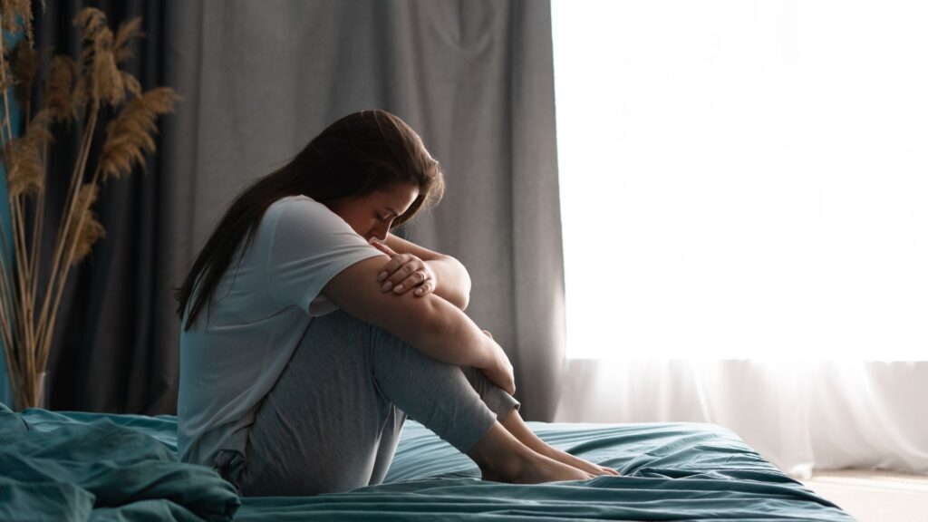 Sad woman sitting on bed in bedroom with light from window. Abuse concept